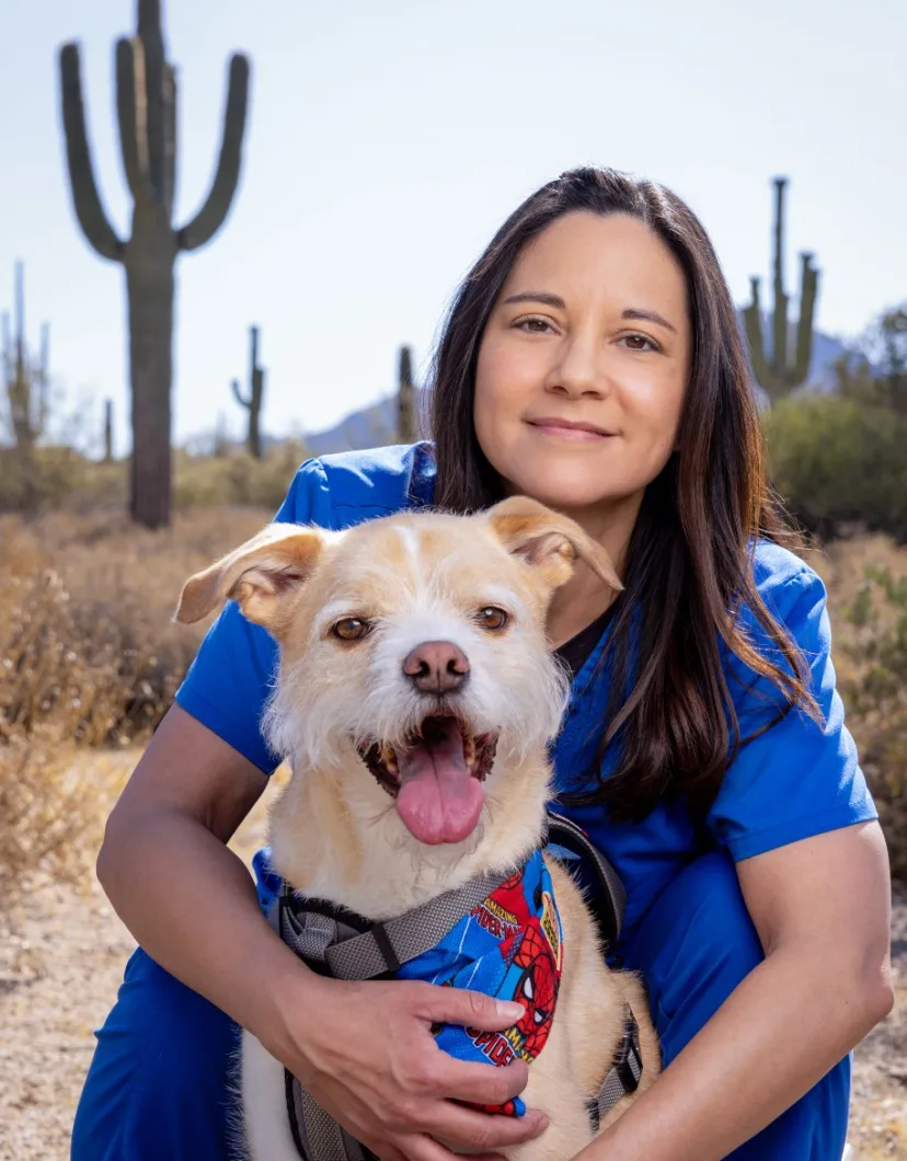 Jennifer in blue scrubs at a desert hugging a dog.